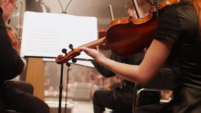 girl and men play violins on stage in colored light