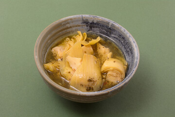 Marinated artichoke hearts in marinade in ceramic bowl on green background