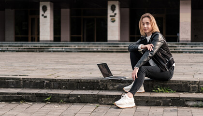 Blonde girl is resting after working on a laptop on the steps in the city.