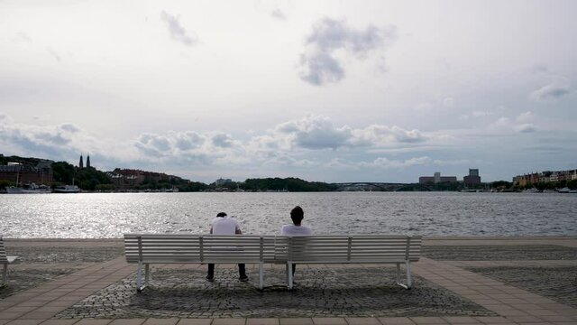 Couple sitting on a bench in front of water body 