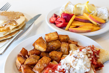 Breakfast on White Table with Potatoes, Crepes, and Sliced Fruit