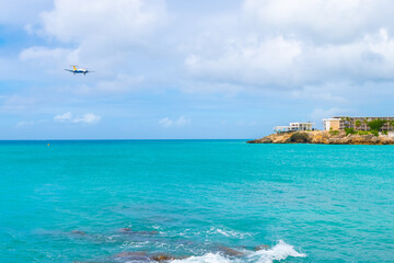 Fototapeta na wymiar Twin turboprop commuter aircraft prepares to land over tropical Caribbean island coast beach.