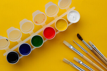Containers with multi-colored paint on a yellow background and brushes of different sizes for...