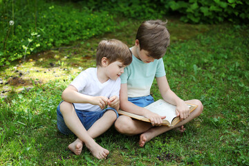 Naklejka na ściany i meble Two brothers are reading a book on the grass
