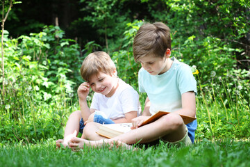 Naklejka na ściany i meble Two brothers are reading a book on the grass