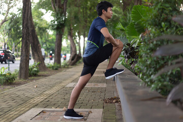 asian young fitness man runner do a stretching leg before running at the park