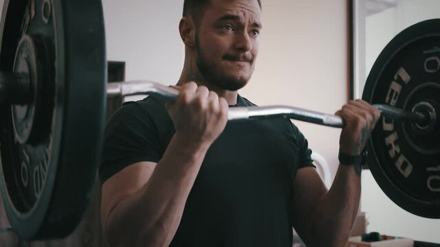 Strong and focused man lifts bar in standing bicep curl, slow motion