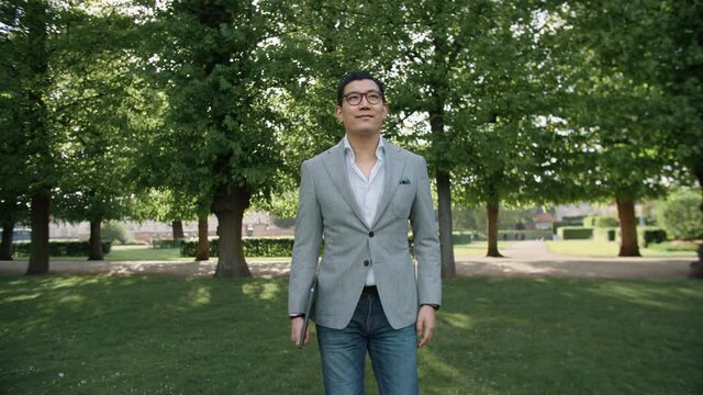 Asian Business Man in Sport Coat Walking Through Park with a Laptop.