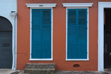 Two windows with blue wooden sash door with shutters on red wall 