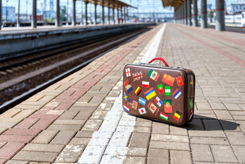Little retro traveler suitcase on a passenger platform. Empty train station.