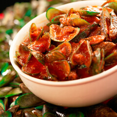 Green mussels cooked spicy with chili sauce in a bowl, placed on a pile of green mussels.