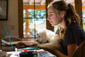 teen age girl holding her English Cream Golden Retriever puppy as she types on her laptop computer