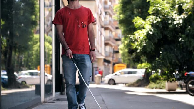 young blind man walking on the sidewalk with the help of his stick