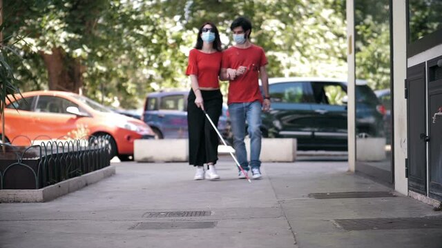 young blind woman walking arm in arm with her boyfriend wearing mask 