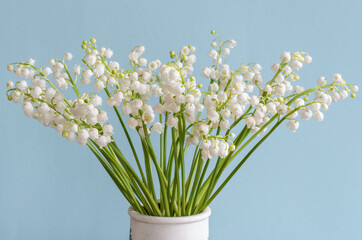  Flowers of lily of the valley (Convallaria majalis), small white bells in a vase on a turquoise background.