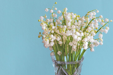  Flowers of lily of the valley (Convallaria majalis), small white bells in a vase on a turquoise background.