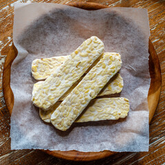 Raw tempeh or tempe, traditional Indonesian soy product on a wooden tray. Top view. Square image. Bali, Indonesia.