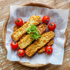 Fried tempeh or tempe (traditional Indonesian soy product), cherry tomatoes and parsley on wooden surface. Top view. Square image.