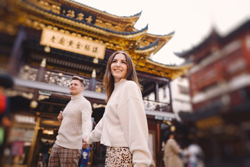 newlywed couple showing affection in Shanghai near Yuyuan. Couple take a break for some hugs while visiting China. husband and wife holding hands on the street by a market and pagoda