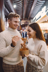 newlywed couple eating noodles with chopsticks in Shanghai outside a food market near Yuyuan. Couple eating authentic local food. husband and wife eating chinese food outisde of a food hall