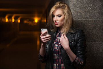 Young fashion blonde woman in leather jacket calling on cell phone