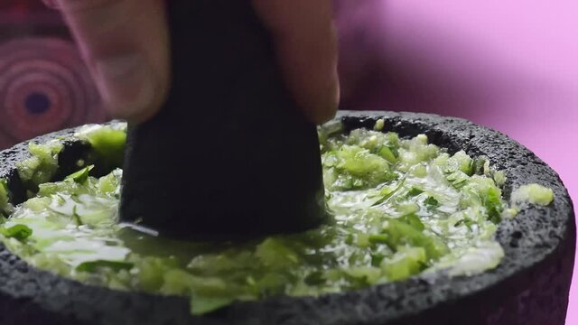 Homemade raw salsa verde, Mexican cuisine. Raw green chili sauce in molcajete, smashed with a tejolote and stirred with a spoon, on pink background