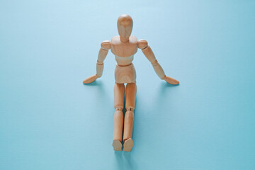 青背景で足を伸ばして座っている木製のモデル人形【正面　ハイアングル】