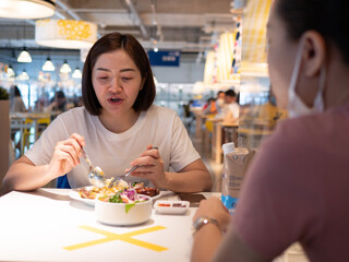 Asian woman sitting separated in restaurant eating food with table shield plastic partition to protect infection from coronavirus covid-19