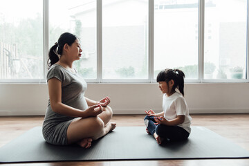 An Asian pregnant woman and child are doing yoga