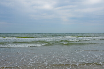 Sea shore landscape on summer cloudy day. Small waves roll onto a sandy beach.