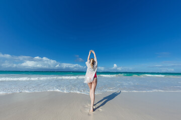 Woman back view relaxing on the sandy beach enjoying sunny day on the tropical caribbean island landscape with turquoise sea and blue sky 