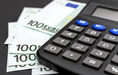 One hundred euro banknotes with calculator on black.