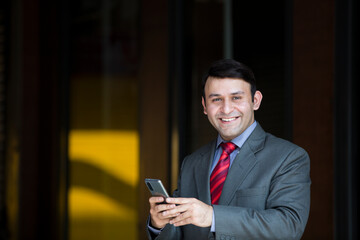 Obraz na płótnie Canvas Smiling businessman with smart phone outdoors on the street, with copy space.New lower prices High-quality images for all your projects ₹345 for this image ₹170 with a 1-month subscription 10 images