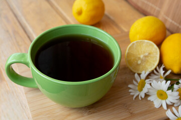 morning Cup of black tea with lemons and chamomile flowers on a wooden table