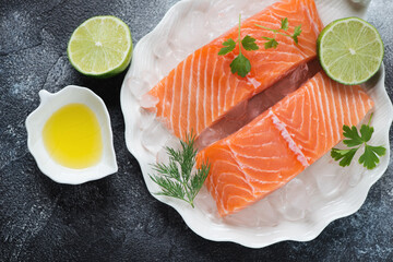 Raw fresh salmon fillet slices on ice with seasonings, above view on a dark-grey stone background, horizontal shot