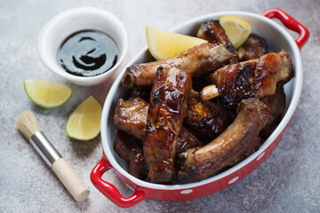 Bowl of chopped roasted pork ribs glazed in honey and soy sauce, studio shot on a beige stone surface