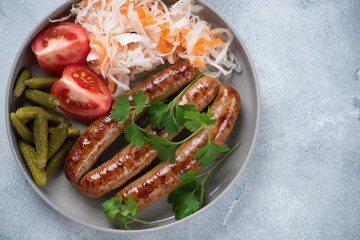 Top view of bbq sausages with sauerkraut, gherkins, tomatoes and parsley, studio shot on a light-blue stone surface with space