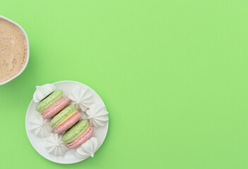 The cup of cappuccino and delicious macarons with white merengues on white plate  on green background. Happy day, breakfast, good morning concepts. Greeting card. Flat lay style with copy space.