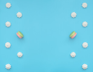Delicious white merengues with one macarons among them on blue background. Happy day, breakfast, good morning concepts. Time for tea. Greeting or invitation card. Flat lay style with copy space.