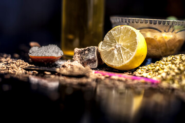 Close up of mung dal soup in glass bowl along with entire constituents with it which are mung bean,green gram, asafoetida, cumin, green chili, black peppercorns, lemon juice and salt on black surface.