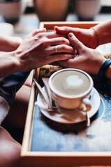 The couple in the cafe holds hands gently. A cup of coffee.