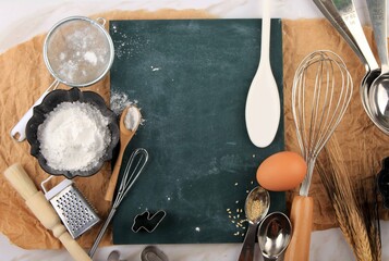 Top View Baking Preparation Background with Baking Ingredients such as Egg, Sesame Seed, Flour, Oil, and Baking Utensils. Suitable for Background or Wallpaper, Copy Space on Center Green Board