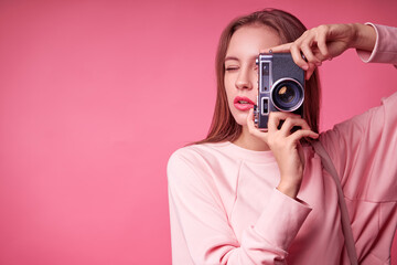 Traveler and photographer. Studio portrait of pretty young girl holding photocamera. Pink blackground.