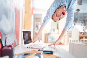 Hard work concept. Technology and business. Stressed young woman hanging upside down over desktop.