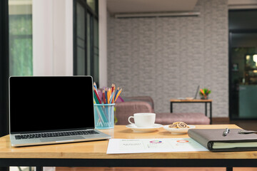 Laptop with blank screen, pencils, vase on table in home office. Workspace with laptop and office supplies.