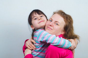a mother with blond hair and her daughter are smiling and hugging. posing for the camera
