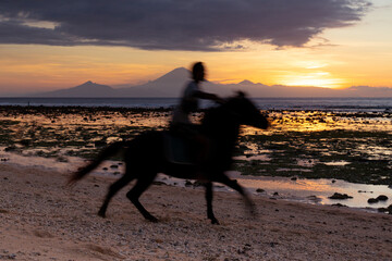 A man galloping on his horse on the beach at sunset on Gili Air, an Island next to Bali.  