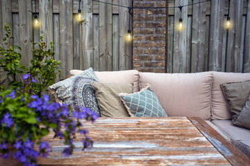 Stylish outdoor garden furniture, sofa with cushions and lamps, light bulbs hanging, cozy modern corner on terrace