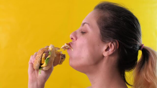 Portrait of caucasian young woman greedily eagerly eating food during quarantine due to coronavirus. Hungry woman on diet laugh and holds in hands big burger. Close up.
