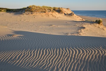 Fototapeta na wymiar Coucher de soleil sur la côte atlantique française, à Soulac-sur-Mer. Les dunes sont striées par le vent. Le paysage est très coloré grâce à la lumière du soleil couchant et à l'océan. Tout est calme.